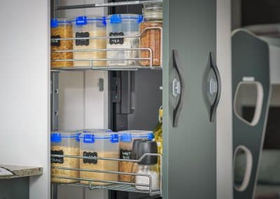 Close-up of pull-out pantry shelving with labelled clear containers of pasta, rice, black tea and rolled oats on top shelf. Bottom shelf shows organic oats, weet-bix, salt and pepper grinders and cooking oil.